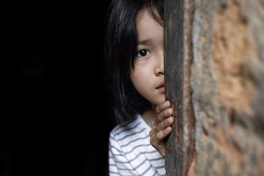 Niño mirando asustado escondido detrás de una pared